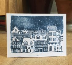 a blue and white card with houses in the background on a wooden table next to a potted plant