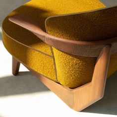 an upholstered yellow chair with wooden arms and back rests against a white wall