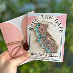 someone holding up a save the date card with a pine cone in it's hand