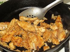 chicken and onions cooking in a skillet with a spatula on the stove top