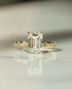 an emerald - cut diamond ring sits on a reflective surface