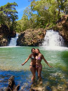 two women standing in the water near a waterfall