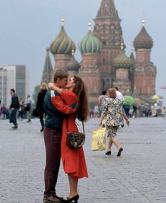 a man and woman kissing in front of a building with domes on it's sides