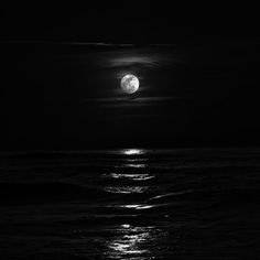 the moon is shining over the ocean at night with dark clouds and water around it