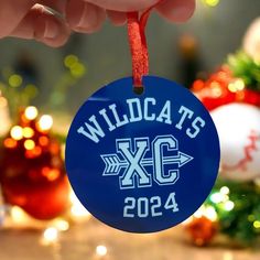 a hand holding a blue ornament with wildcats xc on it