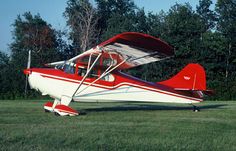 a small red and white plane sitting on top of a lush green field with trees in the background