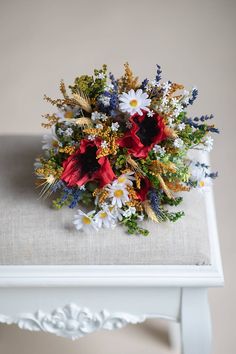 a bouquet of flowers sitting on top of a white table next to a pillow and chair