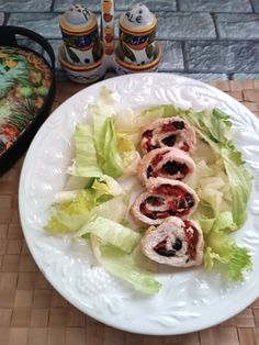 a white plate topped with lettuce wrapped in meat and sauces next to salt and pepper shakers