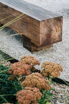 a wooden bench sitting on top of a gravel covered ground next to grass and flowers