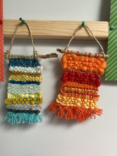 two pieces of beaded art hanging from a wooden frame on a white wall next to a piece of wood