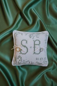 a white pillow with the letter s b on it sitting on a green satin background