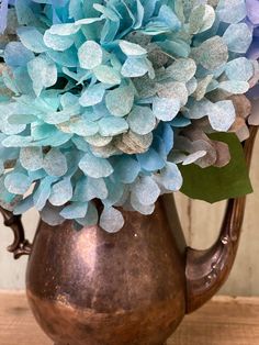 a metal pitcher filled with blue flowers on top of a wooden table