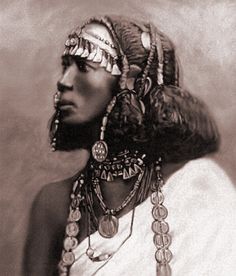 an old photo of a woman wearing headdress and necklaces on her neck