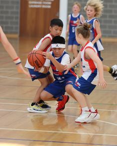 young children playing basketball on an indoor court with other kids in blue and red uniforms