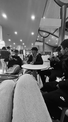 black and white photograph of people sitting at tables in an airport terminal with their feet up on the table