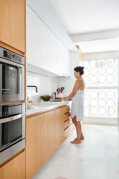 a woman standing in a kitchen next to a stove top oven and an oven door