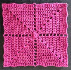 a pink crocheted square with holes in the middle on a gray surface next to a pair of scissors