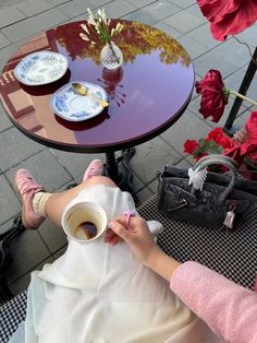 a woman sitting at a table with a cup of coffee in front of her face