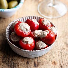 a bowl full of stuffed tomatoes and some olives next to a glass of wine