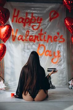 a woman sitting in front of a valentine's day banner holding a cell phone