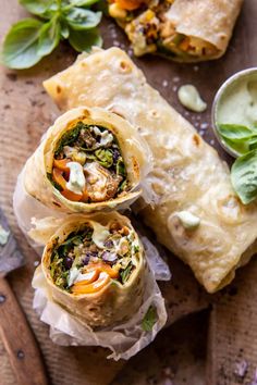 three burritos with different toppings on a cutting board next to dipping sauce