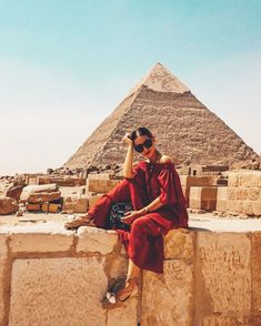 a woman sitting on top of a stone wall next to a large pyramid in the desert