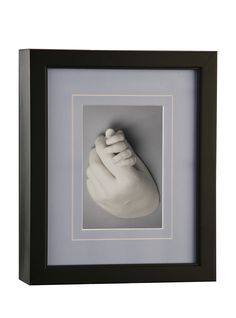 a black frame holds a white sculpture of a baby's foot in the shape of a hand