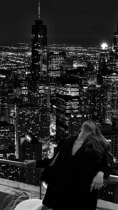 a woman sitting on top of a building in the city at night with her head down