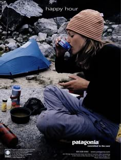 a woman is sitting on the ground drinking from a water bottle and camping gear next to her