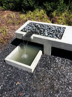 an outdoor fountain with rocks and water coming from it's sides, in the middle of a gravel area