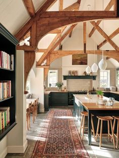 an open kitchen and dining room area with wooden beams on the ceiling, bookshelves in the middle