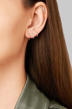 a woman wearing a pair of ear piercings and a green leather jacket with her hair in the wind