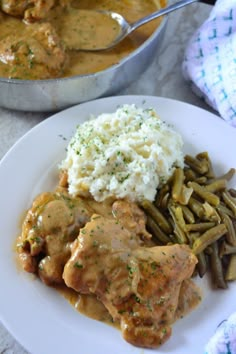 a white plate topped with meat and gravy next to green beans