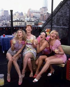 four women sitting on a bench in front of a cityscape and drinking beverages