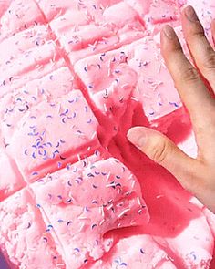 a person's hand reaching for some pink cake with sprinkles on it