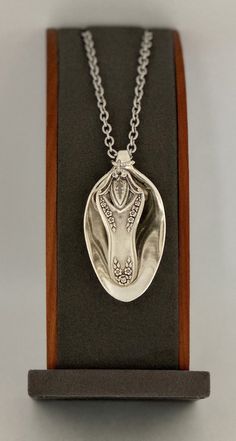 a silver necklace with an animal's head in the center on a wooden stand