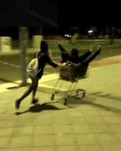 two people pushing a shopping cart down the street