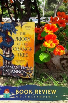 an orange book sitting on top of a lush green field next to red and yellow flowers