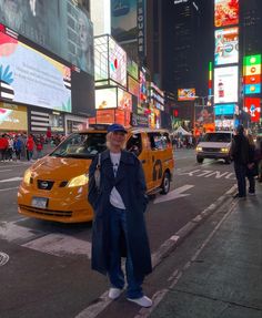 a man standing in the middle of a busy city street at night with taxis and pedestrians