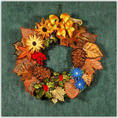 an autumn wreath with sunflowers, leaves and pine cones hanging on a wall