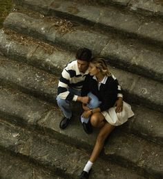 a man and woman sitting on the steps next to each other, looking at each other