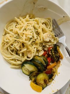 a white plate topped with pasta and veggies next to a knife and fork