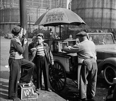 an old black and white photo of three people selling food from a cart on the street