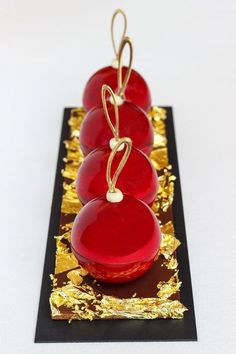 three red apples with gold foil on them sitting on a black and gold plated stand