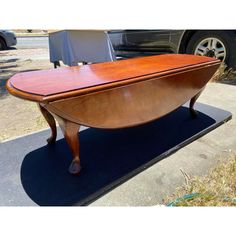 a wooden table sitting on top of a parking lot next to a parked car and another vehicle