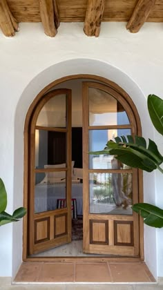 an open wooden door on the side of a white building with potted plants in front of it