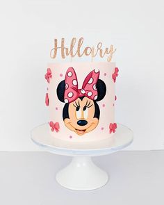 a pink and white cake with minnie mouse on it's face is sitting on a pedestal