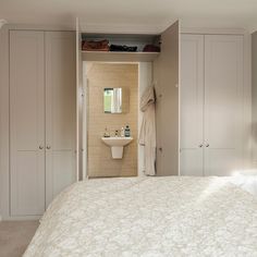 a white bed sitting under a bathroom mirror next to a sink and closet in a bedroom