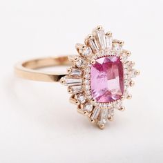 an oval shaped pink sapphire and diamond ring with baguettes on the shoulders, set in yellow gold