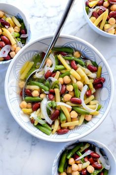 three bowls filled with beans and vegetables on top of a marble countertop next to silver spoons